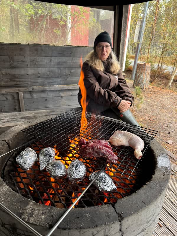 Kött och folieinbakad potatis på gallret över öppen eld i kåtan